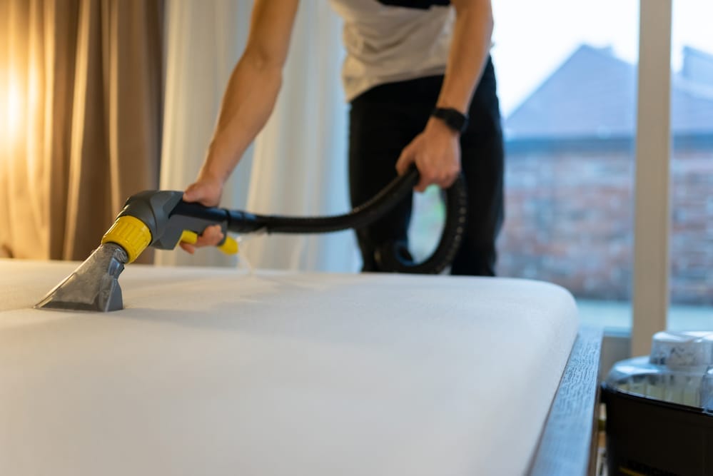 Cleaning mattress with vacuum in bedroom